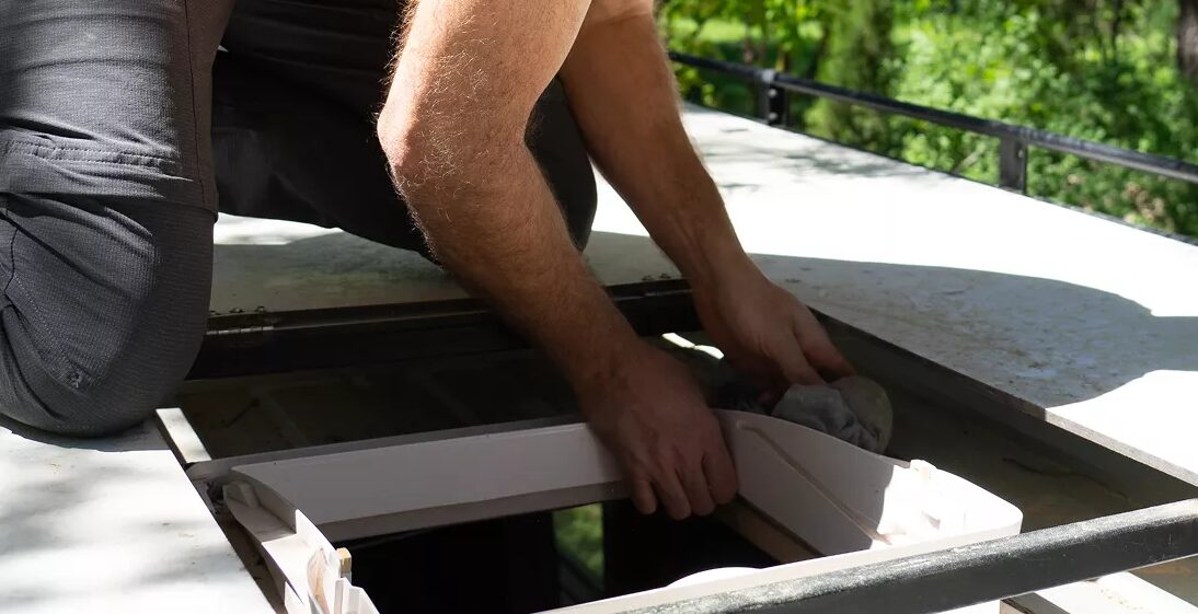 Hands prepping a roof vent opening before coating